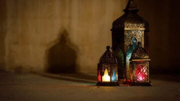 فوانيس مزخرفة بألوان زاهية، تتلألأ في الظلام مع ظلالها على الحائط. تعكس الفوانيس أجواءً دافئة ورمزية، مما يبرز جمال الثقافة العربية.