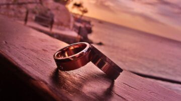 خواتم معدنية متداخلة على حافة خشبية مع غروب الشمس في الخلفية، تظهر ألوان دافئة تعكس جمال المشهد الطبيعي.