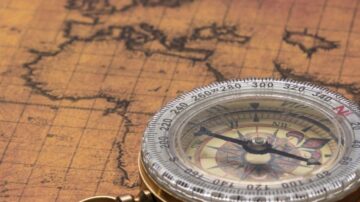 بوصلة تقليدية موضوعة على خريطة قديمة تظهر تفاصيل قارات متعددة. تبرز الألوان الدافئة والخطوط الدقيقة التي تحدد المعالم الجغرافية.