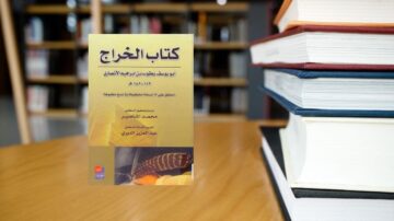 كتاب الخراج لمحمد الجاسر، موضوع في الخلفية المكتبة مع كتب مرتبة. الكتاب يتناول مواضيع الزراعة والاقتصاد الإسلامي.