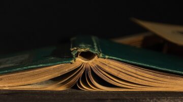 صورة لكتاب قديم يظهر من الزاوية، مع صفحات مفتوحة وحواف ممزقة، الخلفية داكنة. توضح التفاصيل الدقيقة للصفحات الصفراء والتآكل في الغلاف.