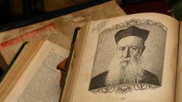 كتاب قديم مفتوح يظهر صورة لرجل ذو لحية بيضاء وعمامة، مع نصوص مكتوبة باللغة العربية، محاط بمجموعة من الكتب القديمة.