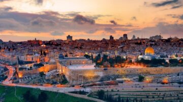 غروب الشمس فوق مدينة القدس، تظهر قبة الصخرة في المقدمة مع أضواء المدينة تتلألأ في الخلفية، مما يعكس جمال التاريخ والمعمار في المنطقة.