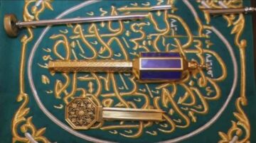صورة لقطعة فنية تتضمن مفاتيح ذهبية وزخارف عربية، مع خلفية خضراء مكتوبة بخط عربي. التصميم يتضمن نصوص دينية وزخارف تقليدية، مما يعكس الثقافة الإسلامية والفن العربي.