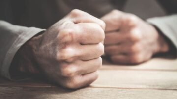 أيد مشدودة تعبّر عن الغضب أو التوتر، مع خلفية خشبية. تعكس الصورة مشاعر القلق والاحتدام.