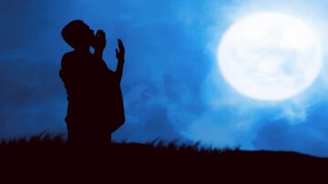 رجل يقف silhouetted أمام قمر مكتمل في سماء زرقاء، مع تعبير تأملي، مما يخلق جوًا من الهدوء والسكون.