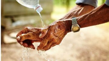 يد تُسكب عليها مياه من زجاجة، تُظهر عروقاً وتجاعيد، بينما تتدفق المياه على يدٍ أخرى. تعكس الصورة لحظة من العناية أو النظافة مع التركيز على التفاصيل الدقيقة للجلد والماء.