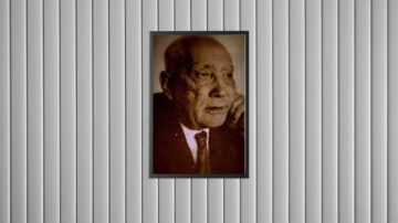 صورة بالأبيض والأسود لرجل في منتصف العمر يظهر بملامح جدية. يرتدي بدلة وربطة عنق، ويضع يده على خده. الصورة مؤطرة وتظهر على جدار ذو تصميم عمودي.