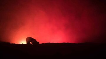 صورة ظلية لشخص ينحني أمام ضوء أحمر مشع وسط دخان كثيف، مما يخلق جوًا غامضًا ومثيرًا.