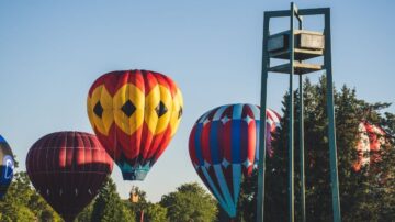 بالونات هوائية ملونة ترتفع في السماء الزرقاء، مع وجود هيكل معدني في الخلفية. تتنوع الألوان والتصاميم بين الأحمر والأصفر والأزرق. المنظر يعكس جمال الفعاليات الخارجية وتجربة الطيران.