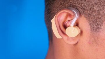 صورة توضح سماعة أذن ملحقة بالأذن، تظهر تفاصيل السماعة بلون بيج وخلفية زرقاء. التركيز على تصميم السماعة وطريقة تركيبها.