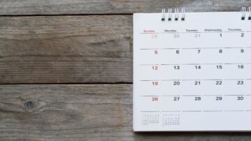 تقويم ورقي لشهر يحتوي على تواريخ وأيام الأسبوع، مع تصميم بسيط وألوان محايدة، موضوع على سطح خشبي.