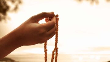 يد تحمل سبحة برتقالية، تُظهر التركيز والسكينة، مع خلفية ضبابية توحي بالهدوء والروحانية.