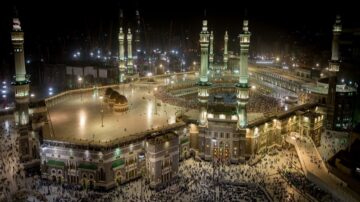 صورة لمدينة مكة المكرمة في الليل، تُظهر الكعبة المشرفة محاطة بالحجاج في الساحة. الأضواء تضيء المعالم الإسلامية الشهيرة، بما في ذلك المساجد والمآذن، مما يبرز جمال المكان وأهميته الروحية.