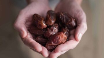 تمر طازج في يدي شخص، يظهر تفاصيل قوامه اللزج ولونه الغني، مع خلفية طبيعية.