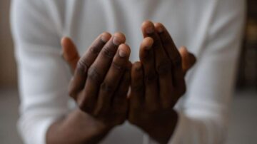 يدين مفتوحتين لشخص من أصول أفريقية، تظهر تفاصيل الأصابع والجلد بلون دافئ، تعبير عن الاستعداد أو الدعاء في بيئة هادئة.