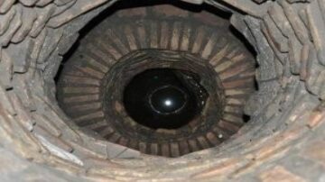 صورة توضح عمق بئر مبني من الطوب، يظهر في الأسفل كرة داكنة تعكس الضوء. الجدران الداخلية للبئر مصنوعة من الطوب، مما يبرز التفاصيل الهندسية.