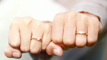 صورة ليدين متشابكتين، تحمل إحداهما خاتم خطوبة مزين بألماس، بينما تحمل الأخرى خاتم زفاف بسيط. تعكس الصورة رمزية الحب والارتباط.