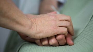 يدين تُمسكان ببعضهما في مشهد يعبر عن الدعم والراحة، مع التركيز على التفاصيل الدقيقة للجلد. تعكس الصورة مشاعر الألفة والاهتمام في سياق الرعاية الصحية.