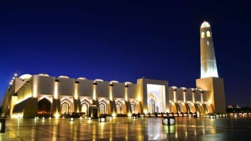 مسجد في ظلمة اليل مع اضاءة خفيفة مبهرة وانعكاس الضور على بلاط الساحة الخاصة بالمسجد