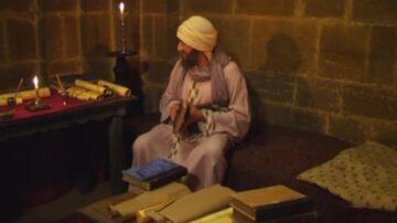 رجل يجلس في غرفة ذات جدران حجرية، محاط بكتب ومخطوطات، مع شموع مضاءة على الطاولة. يرتدي ثوباً تقليدياً وعمامة، ويبدو وكأنه في حالة تفكير عميق.
