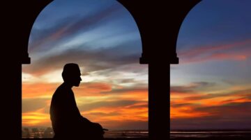 صورة ظلية لرجل جالس تحت أقواس، مع غروب الشمس الملون في الخلفية. السماء مزيج من الألوان الدافئة، مما يخلق مشهدًا هادئًا وتأمليًا.