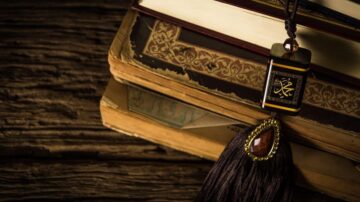 كتب قديمة موضوعة على سطح خشبي، مع تعليقة مزخرفة تحمل رموزاً شرقية، تتدلى من إحدى الكتب وتضيف لمسة فنية.