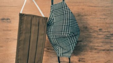 قناعان وجه معلقان على خلفية خشبية، أحدهما بلون بني والتاني بنمط متداخل باللونين الأبيض والأسود، يمثلان خيارات للوقاية من العدوى الصحية.