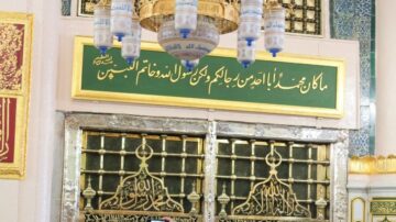 نقش عربي على لوحة جدارية في مكان تاريخي، يبرز الآيات القرآنية والعبارات الدينية، مع أبواب مزخرفة وزخارف تقليدية. تعكس الصورة العمارة الإسلامية والتراث الثقافي.