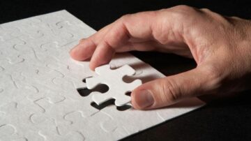 يد تمسك قطعة بازل بيضاء وتضعها في مكانها المخصص على لوح بازل، مع خلفية داكنة تبرز تفاصيل القطعة.