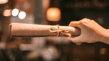 يد تحمل لفافة ورقية مربوطة بخيط، تظهر خلفية ضبابية لمكان داخلي دافئ مع إضاءة خافتة.