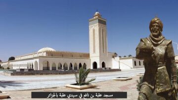 مسجد عتبة بن غزوان في سيدي عتبة بالجزائر يظهر تصميمه المعماري الفريد مع مئذنته العالية. تمثال تاريخي لشخصية بارزة يقف في المقدمة، مما يعكس التراث الثقافي للمنطقة.