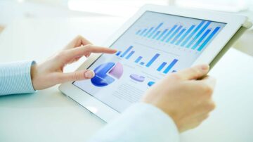 رجل يستخدم جهاز لوحي لعرض بيانات الرسوم البيانية والمخططات. تظهر الرسوم البيانية بألوان زرقاء ووردية، مع مؤشرات مختلفة تعكس الأداء والتحليل.