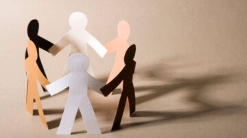 أشخاص ورقيون ملونون بألوان متنوعة، يمثلون التنوع والتضامن، يقفون في دائرة ويمسكون بأيدي بعضهم البعض، مع ظلال تظهر على الخلفية البنية.