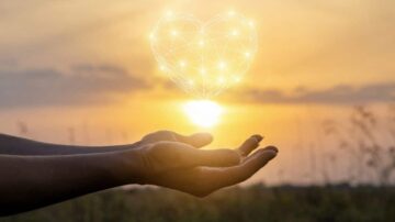 يدين ترفعان نحو السماء مع قلب مضيء متكون من خطوط متصلة، في خلفية غروب الشمس. تعكس الصورة مشاعر الحب والأمل.