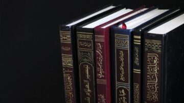 مجموعة من الكتب ذات الأغلفة الملونة، تتنوع بين الأسود والأحمر، موضوعة بشكل عمودي على خلفية داكنة. الكتب تحمل عناوين باللغة العربية، مما يعكس محتوى أدبي وثقافي غني.
