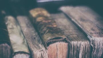 كتب قديمة متراصة على رف، تظهر تفاصيل الغلاف والتآكل على الحواف، تعكس تاريخًا وتراثًا أدبيًا غنيًا.