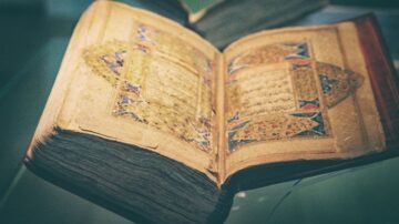 كتاب قديم مفتوح يظهر نصوصًا مزخرفة، مع صفحات ذات حواف داكنة وتصميم معقد. يعكس التراث الثقافي والفني للكتاب الإسلامي.