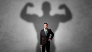 رجل في بدلة رسمية يحمل حقيبة، يظهر خلفه ظل قوي يشير إلى قوة وثقة.