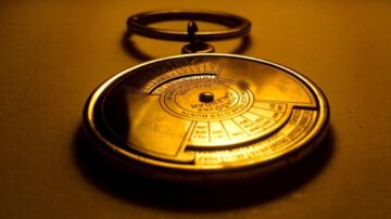 ساعة جيب معدنية قديمة مع حلقة معدنية، تظهر بإضاءة دافئة، تحمل تفاصيل دقيقة على وجهها، مثل الأرقام والرموز، مما يبرز تصميمها الكلاسيكي.