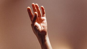 يد مرفوعة بأصابع مفتوحة على خلفية دافئة، تعبر عن الإشارة أو الدعوة.