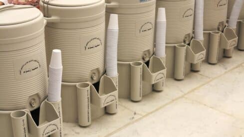 Zamzam water storage containers with plastic cups on a marble floor.