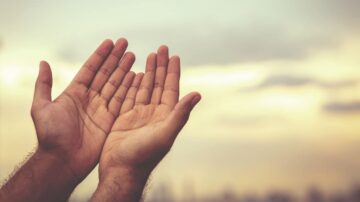 أيدي مرفوعة إلى السماء في وقت الغروب، تعبر عن الأمل والدعاء، مع خلفية غائمة تخلق جوًا من السكينة والتأمل.