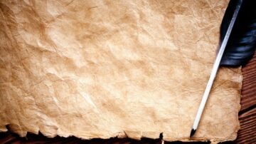 ورقة قديمة متموجة بلون بني، بجوارها قلم ريش أبيض. تعكس الصورة أجواء الكتابة التقليدية والتاريخية.
