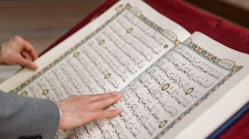 كتاب مفتوح يحتوي على نصوص باللغة العربية، يُظهر يدًا تلامس الصفحة، مع تصميم مزخرف حول النص.