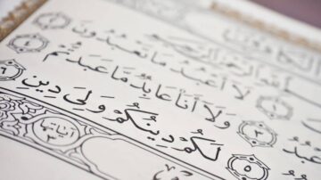 نص عربي مكتوب بخط جميل من القرآن الكريم، يظهر آيات مرتبة مع تزيينات هندسية حول الحواف. التركيز على جمال الخط والتفاصيل الفنية.