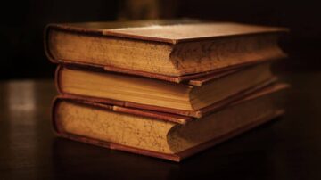 كتب قديمة متراكمة على طاولة، تظهر تفاصيل الغلاف والتجاعيد على الصفحات. الإضاءة الخافتة تضيف جوًا من الأصالة والحنين.