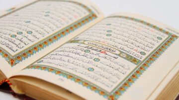 صفحة مفتوحة من كتاب القرآن الكريم، تظهر النص العربي المكتوب بخط جميل وتزيين ملون حول الحواف، مما يعكس جماليات التصميم الإسلامي.