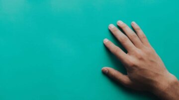 يد ممدودة على سطح أزرق فاتح، تركز الضوء على تفاصيل الأصابع والجلد.