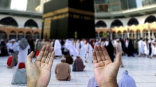 Hands in prayer gesture before the Kaaba, with a crowd gathering in the Grand Mosque, Mecca.